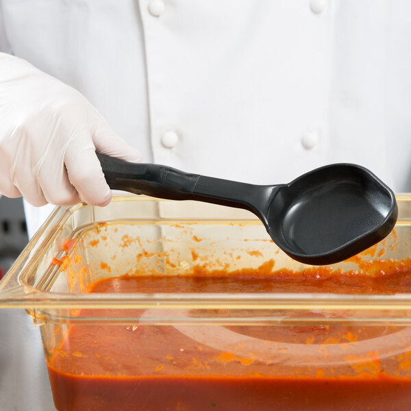 A person in a white coat using a black Vollrath High Heat Solid Oval Nylon Spoodle to serve red sauce.