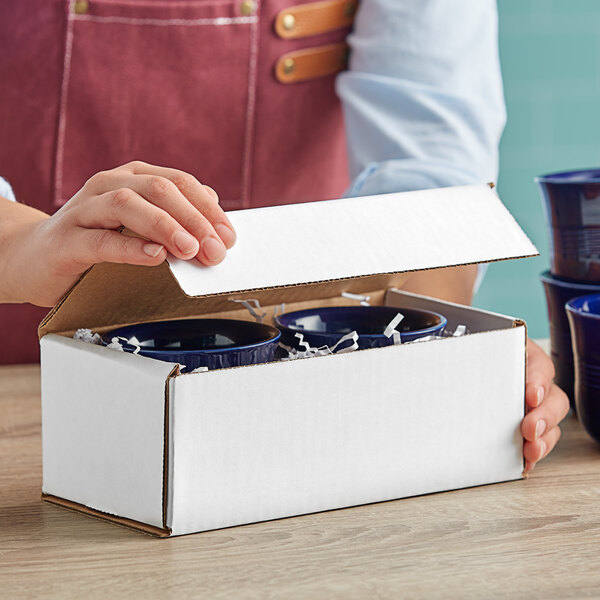A person opening a white Lavex mailer box containing blue cups.