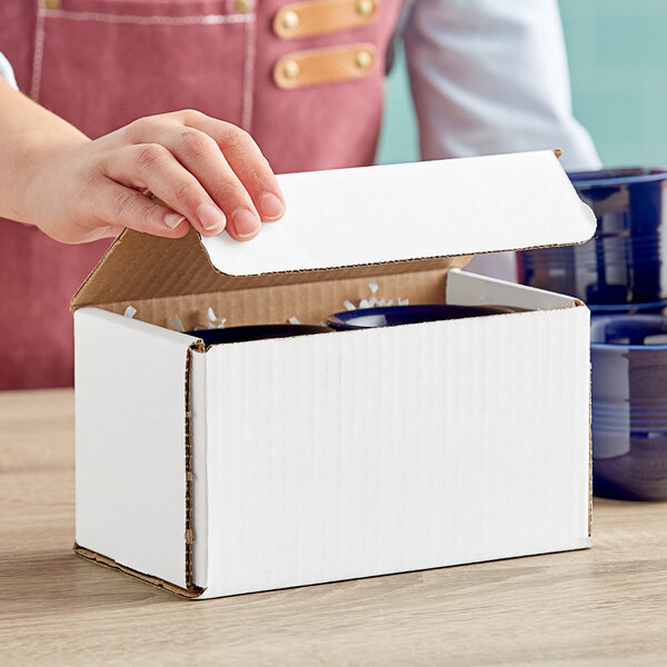 A hand opening a white Lavex corrugated mailer to reveal a blue mug.