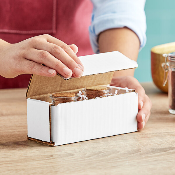 A hand opening a white Lavex corrugated mailer box to reveal small glass jars inside.