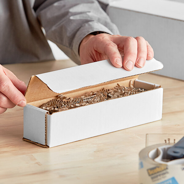 A person opening a white Lavex corrugated mailer box with a screwdriver.