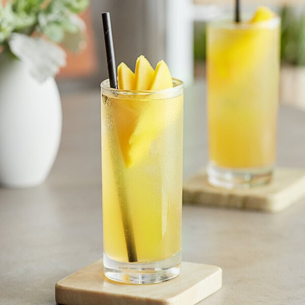 A glass of yellow Tractor Beverage Co. mango juice with a straw.