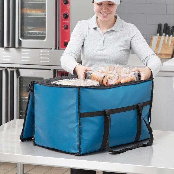 A woman holding a blue Choice insulated food pan carrier full of food.
