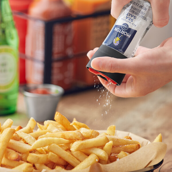 A person using a Morton Sea Salt grinder to salt french fries.