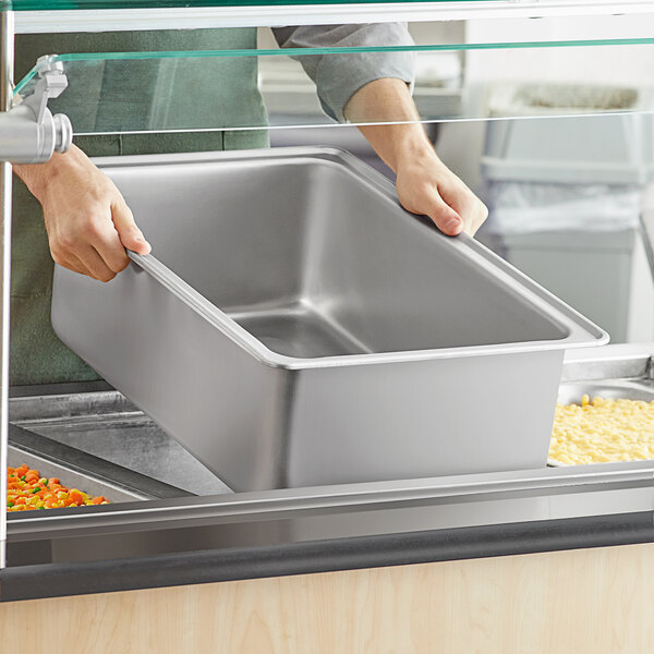 A person holding a Vigor stainless steel steam table spillage pan on a counter.