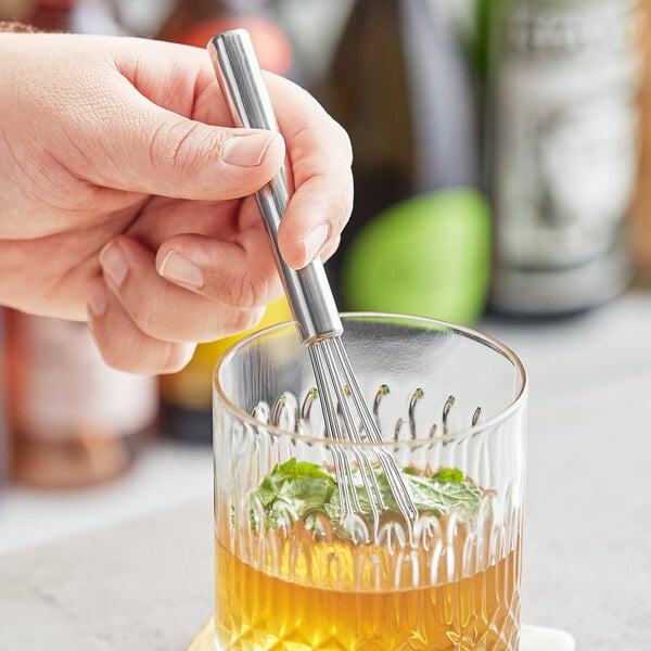A hand using an American Metalcraft stainless steel mini bar whisk to mix a drink.