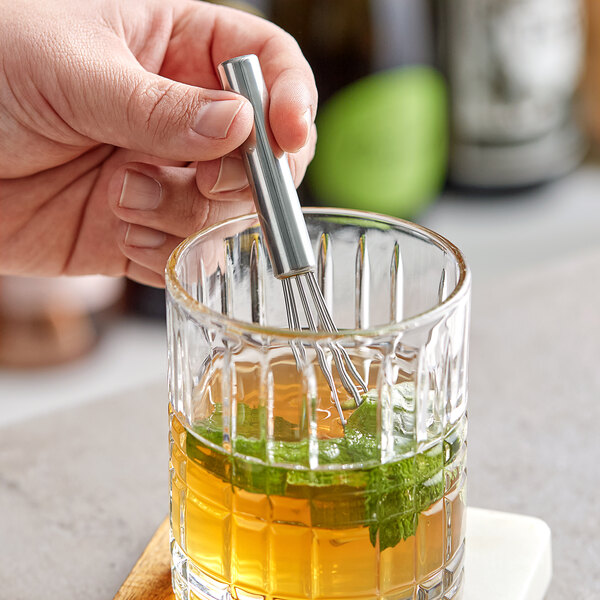 A hand using an American Metalcraft stainless steel mini bar whisk in a glass with a drink.