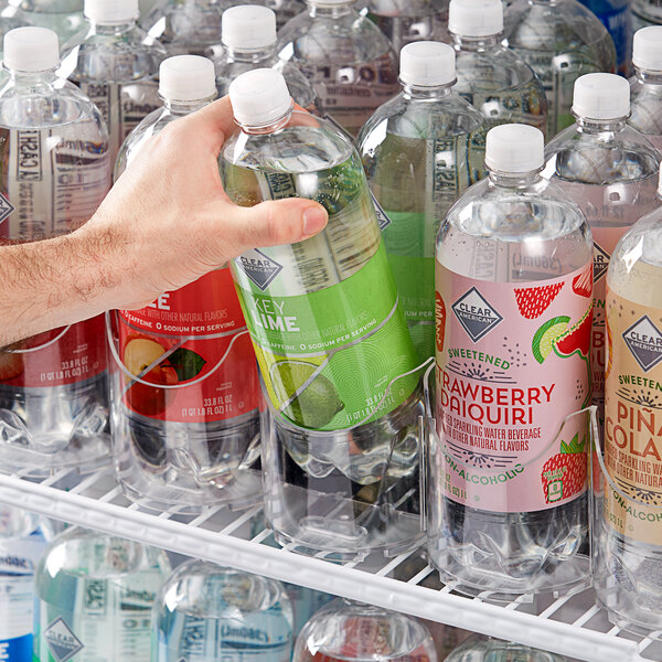 A hand using a 6 Lane Universal Pusher Glide Bottle Organizer to pull out a bottle of soda.