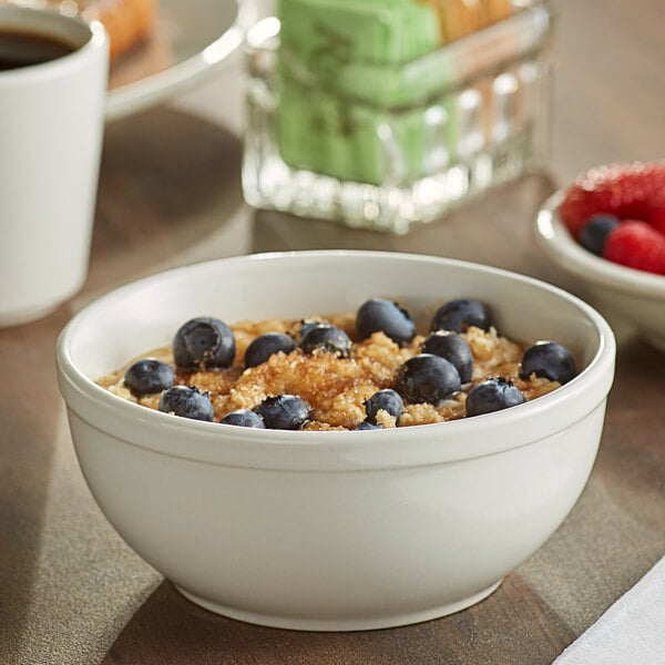 An Acopa ivory stoneware bowl filled with oatmeal and blueberries on a table.