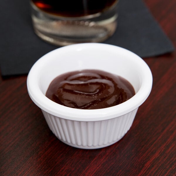 A white fluted ramekin filled with brown sauce on a table.
