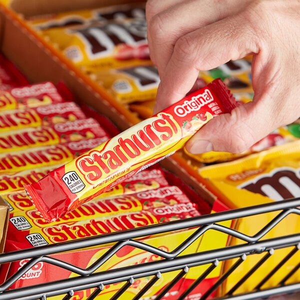 A hand holding a STARBURST® Original Fruit Chews package on a counter.