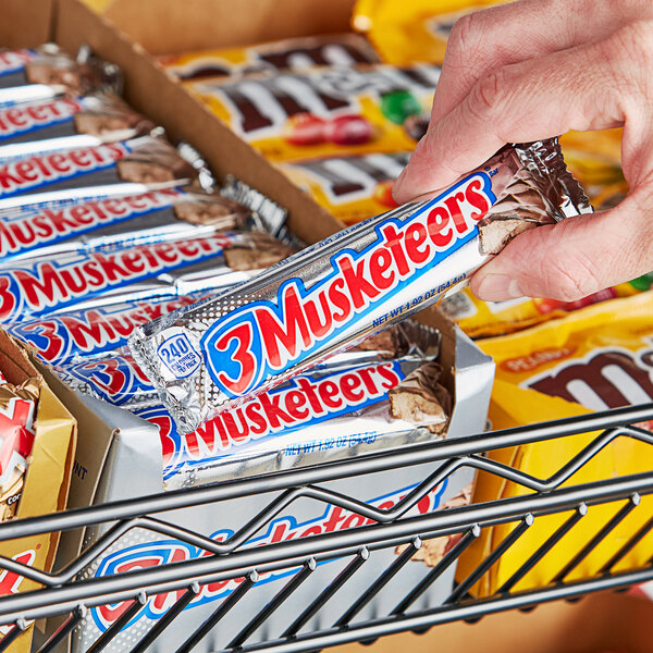 A hand holding a 3 MUSKETEERS chocolate candy bar.