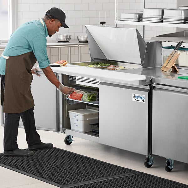 A man in a professional kitchen using an Avantco stainless steel sandwich prep table.