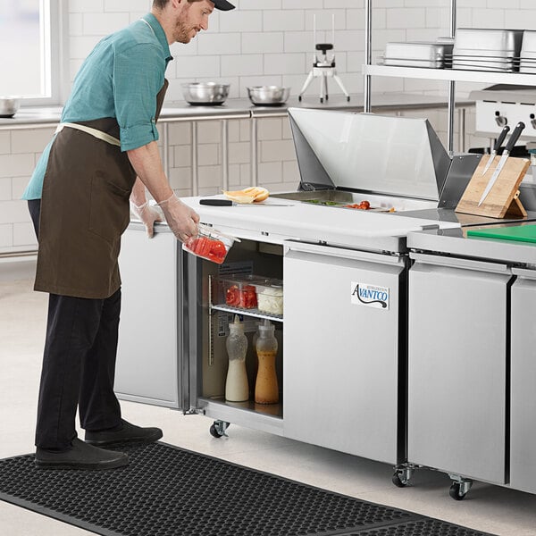 A man in a professional kitchen using an Avantco stainless steel sandwich prep table.
