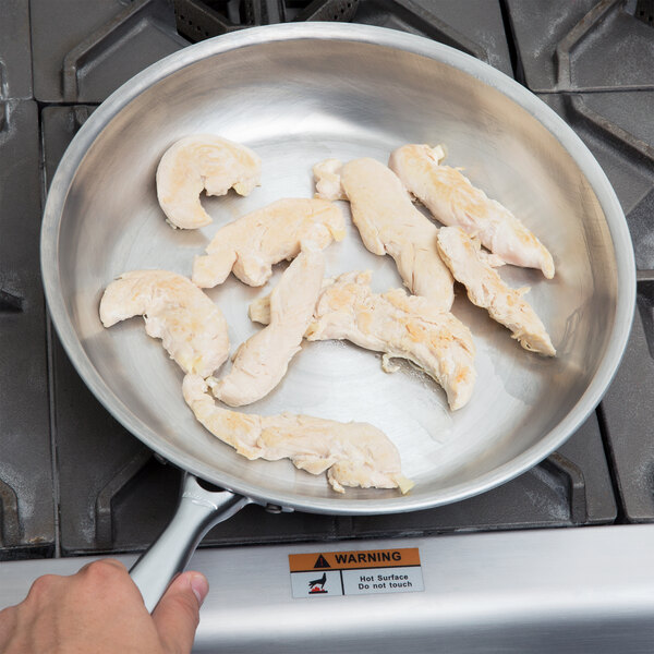 A person holding a Vollrath Wear-Ever frying pan with chicken in it.