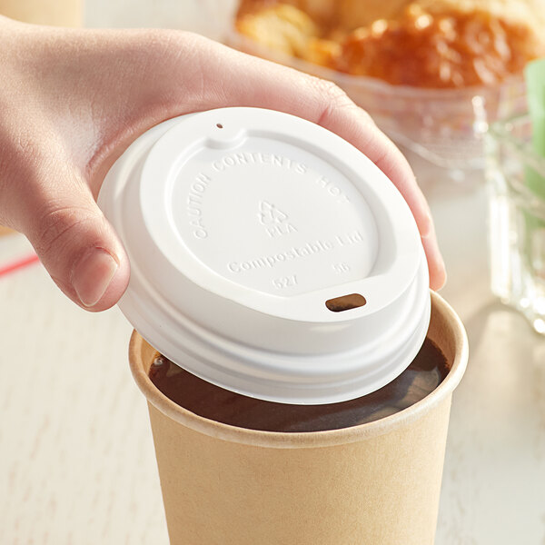 A hand holding a New Roots translucent paper hot cup with a white lid on top.