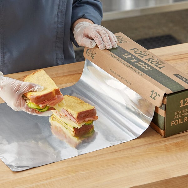 A person in gloves holding sandwiches on a table with EcoChoice aluminum foil.