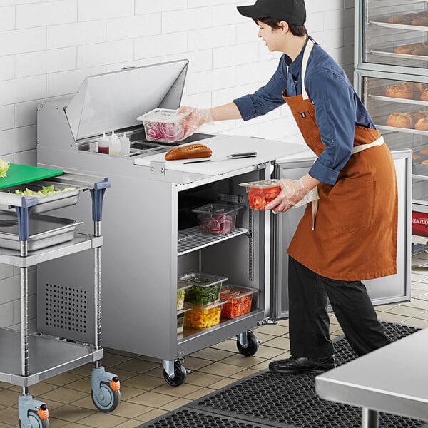 An aproned person using an Avantco sandwich prep table to store food.