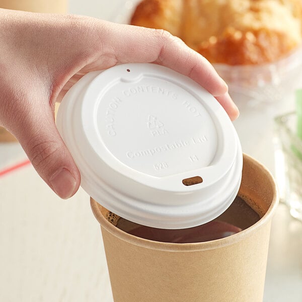 A hand holding a white New Roots compostable paper lid on a coffee cup.
