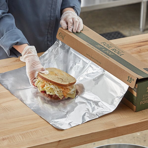 A person wearing gloves putting food on a sandwich with EcoChoice aluminum foil.