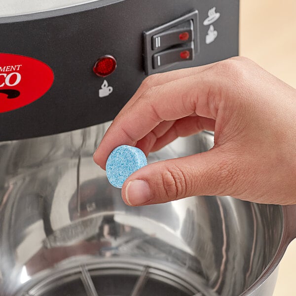 A hand holding a blue round Urnex Tabz Z61 coffee cleaning tablet.