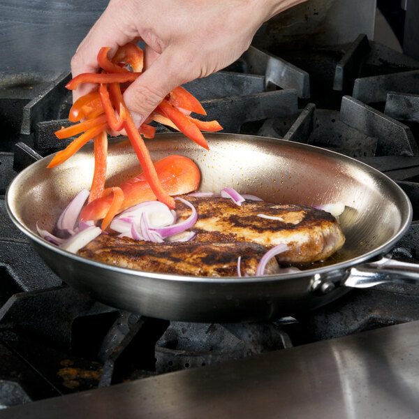 A person cooking food in a Vollrath stainless steel fry pan.