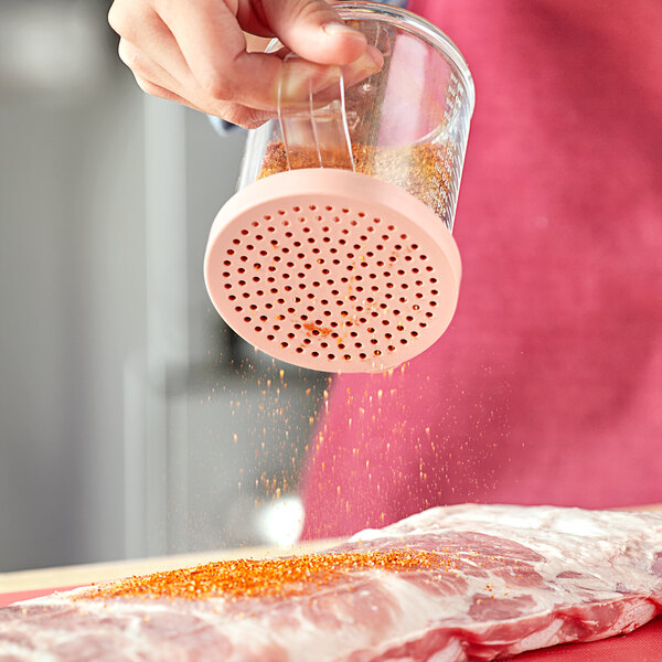 A person using a Choice Rose Lid to sprinkle seasoning on a piece of meat.