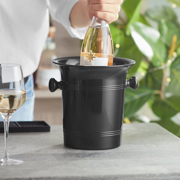 A person pouring wine into a black plastic wine bucket on a table.