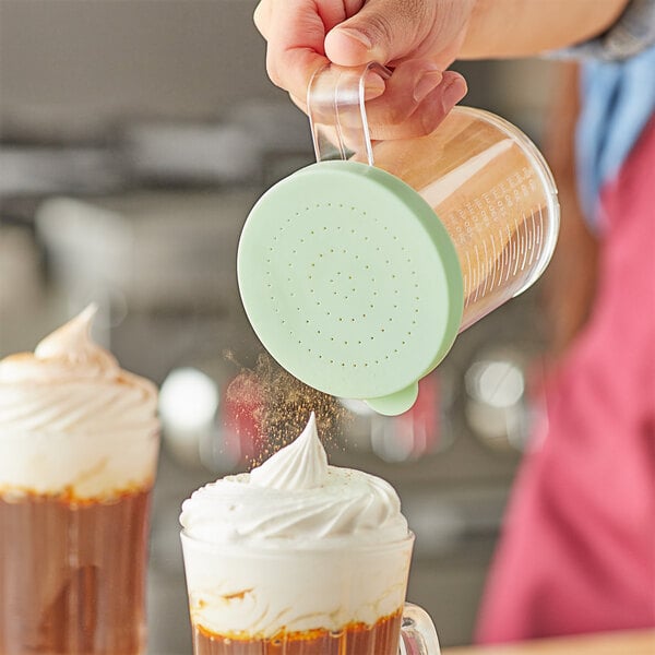A person using a Choice polycarbonate shaker with a green lid to pour finely ground product onto a drink.