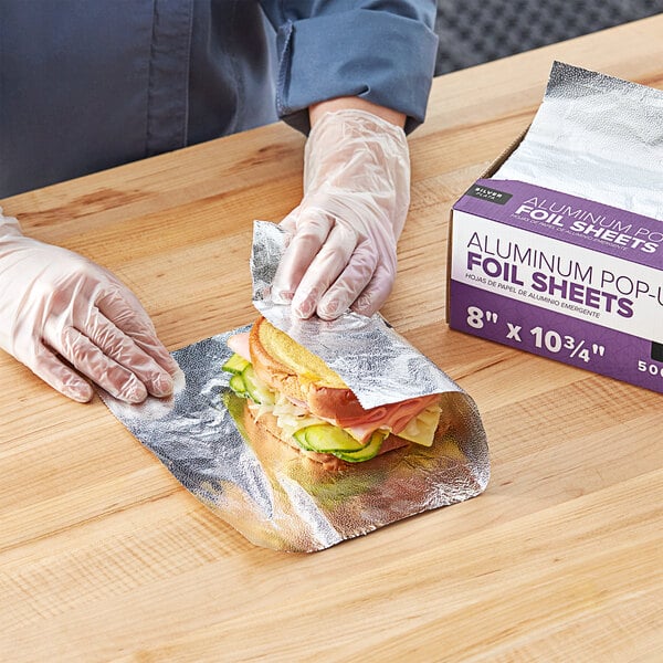 A person wearing gloves is wrapping a sandwich in Choice interfolded foil.