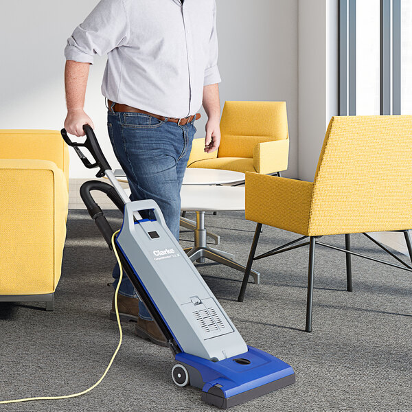 A man using a Clarke CarpetMaster 115 upright vacuum cleaner on a carpet in a corporate office.