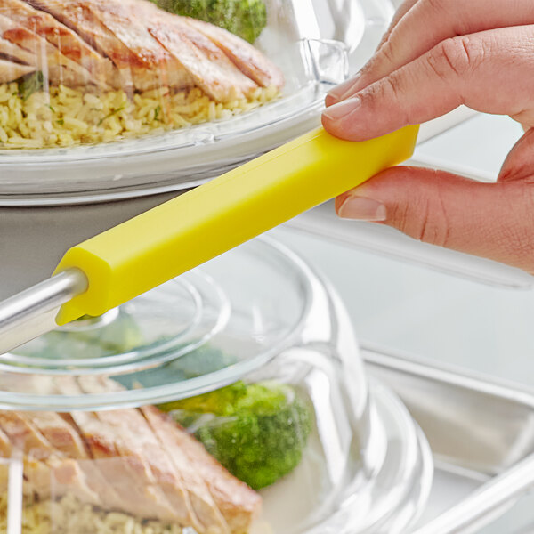 A hand using a yellow Baker's Mark silicone clip to identify food on a tray.