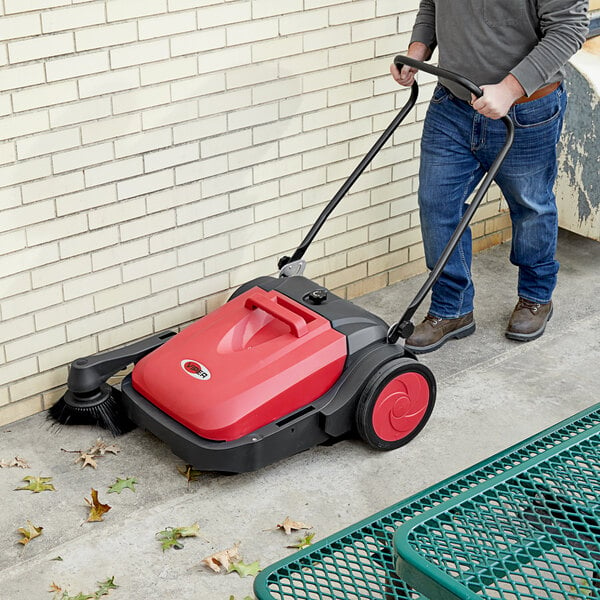 A person pushing a red and black Viper PS480 manual push sweeper.