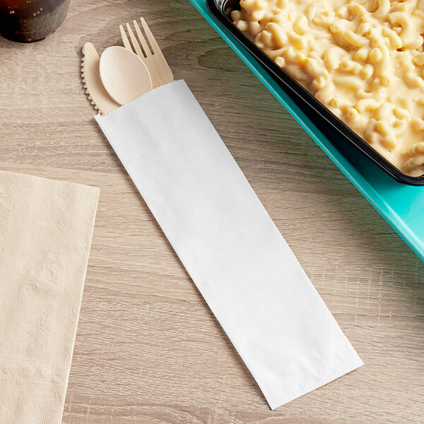 A white Bagcraft paper bag with a tray of macaroni and cheese, a fork, and a spoon.
