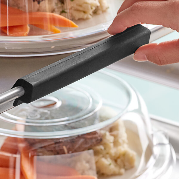A hand holding a black Baker's Mark silicone bun pan clip over a food container.