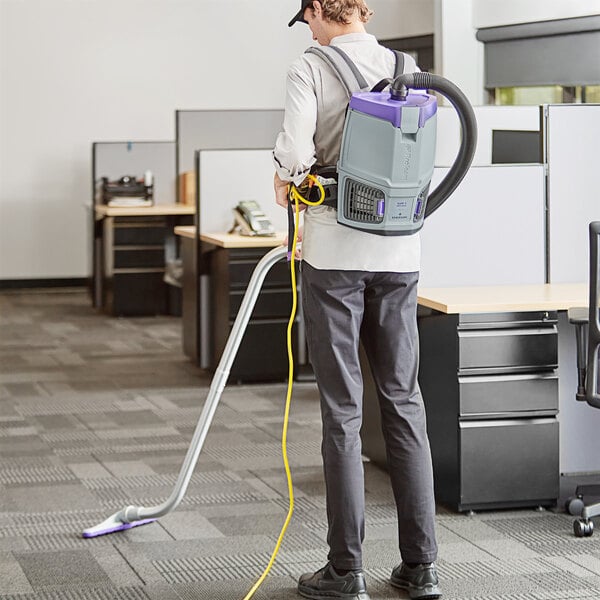 A man using a ProTeam GoFit backpack vacuum with a purple and grey plastic container.