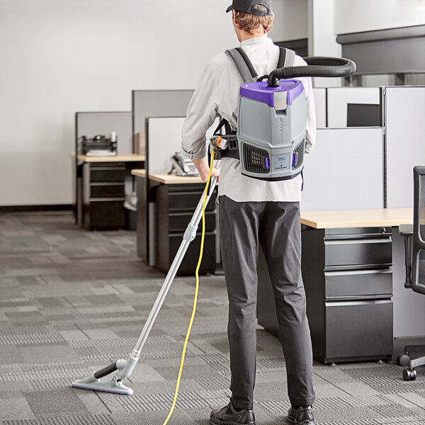 A man with a ProTeam backpack vacuum cleaner vacuuming a carpet in an office.