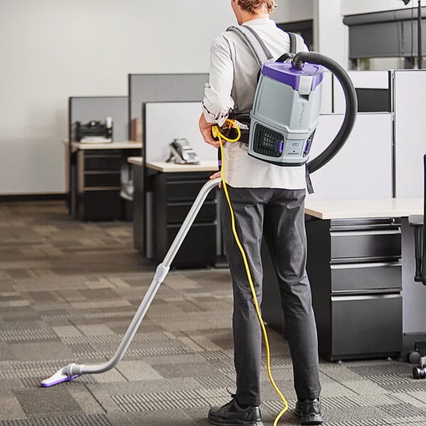 A man using a ProTeam GoFit backpack vacuum in a corporate office cafeteria.