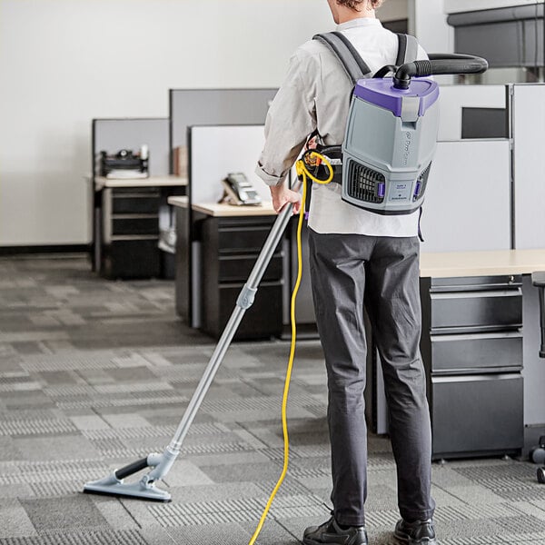 A man wearing a ProTeam GoFit backpack vacuum cleaner in a corporate office cafeteria.