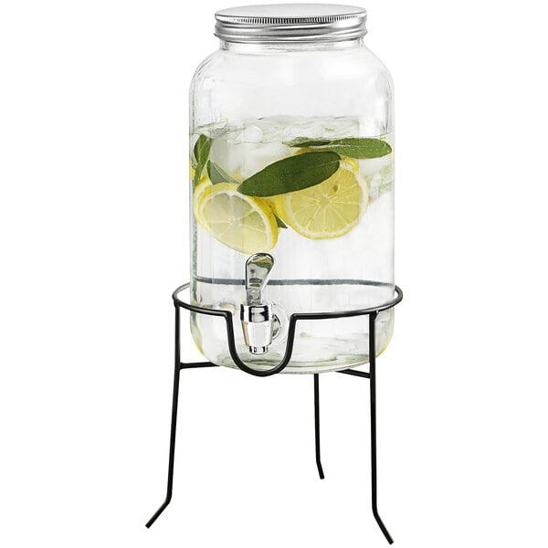 A Stylesetter glass beverage dispenser with water and lemon slices on a stand.