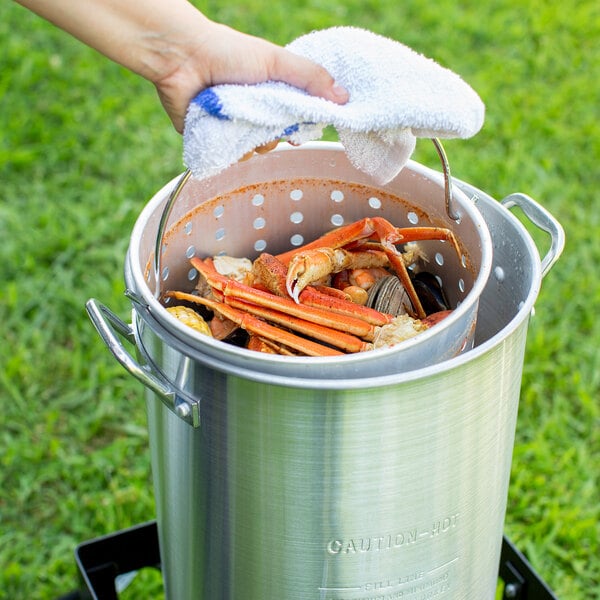A person using a Backyard Pro aluminum seafood boiler to cook a pile of crab legs.