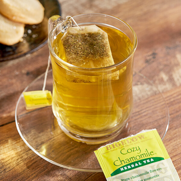 A glass mug of Bigelow Cozy Chamomile Herbal Tea with a tea bag on a plate.