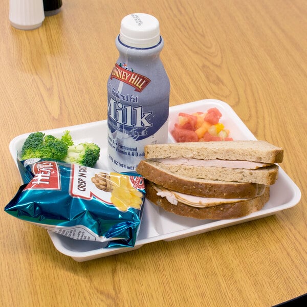 A white Genpak foam school tray with a sandwich, broccoli, chips, and a white milk cup on a table.