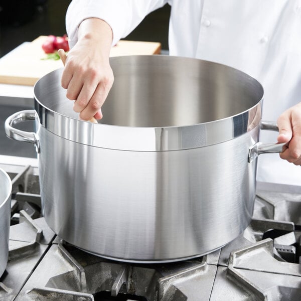 A chef stirring a large silver sauce pot.