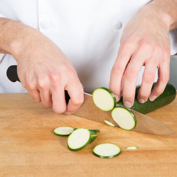 A person using a Victorinox Chef Knife to slice a cucumber on a cutting board.