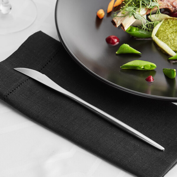 An Acopa Odin stainless steel dinner knife and fork on a white plate with a napkin