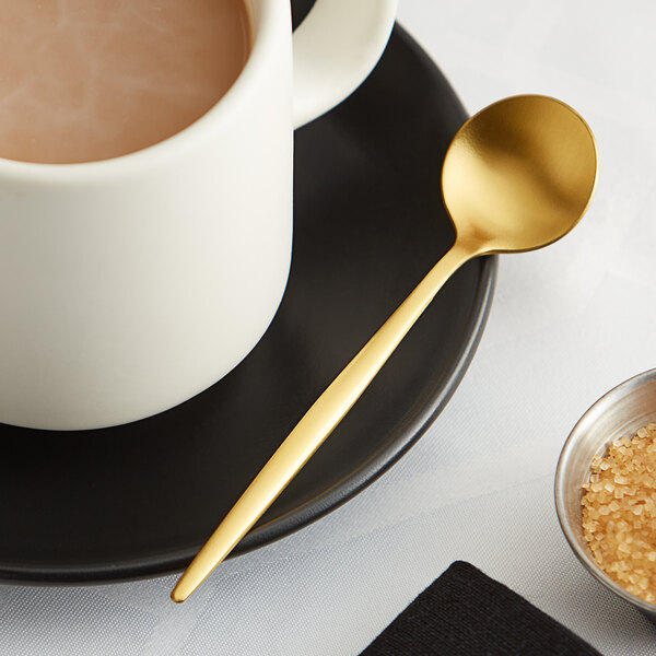 An Acopa Odin stainless steel demitasse spoon on a plate with a cup of coffee and brown sugar.