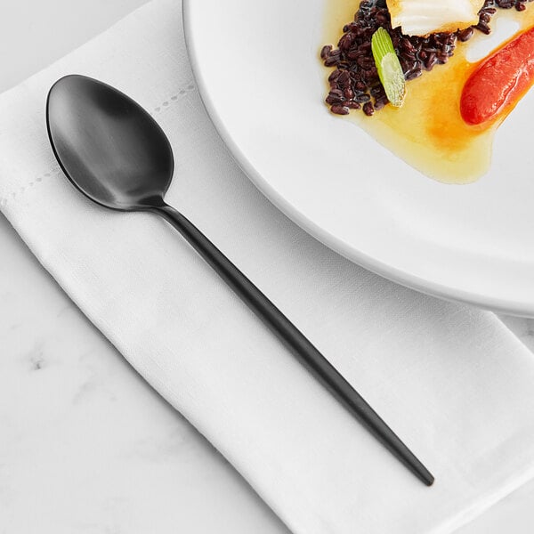 An Acopa Odin stainless steel dinner spoon on a white plate with a napkin