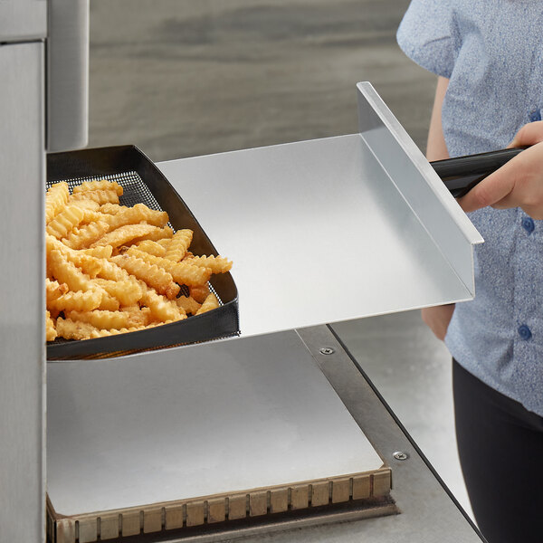 A person using an aluminum paddle peel to remove fries from a rapid cook oven.
