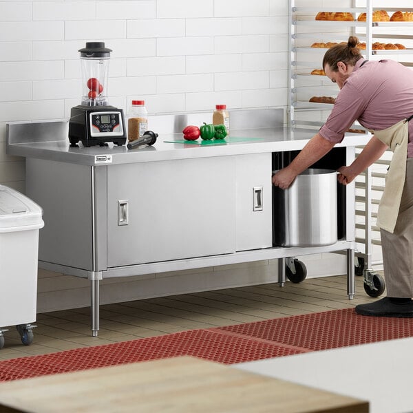 A man using a Steelton stainless steel enclosed base table in a kitchen.